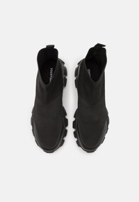 Černé slip-on tenisky s texturovaným pleteným svrškem a tlustými gumovými podrážkami s ostrými vzory pro lepší přilnavost a podporu.