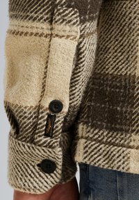 Geknoopte wollen flanellen overhemd met een houndstooth-patroon in roomwit, bruin en donkerbruin. Kenmerkt zich door een gestructureerde stof en een zwarte logo-label detail.