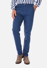 Chinos azzurri in cotone con vestibilità slim, dotati di chiusura frontale con bottone e tasche. Abbinati a scarpe in suede marrone chiaro.