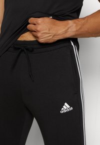 Svarta sportiga joggers med vita sidosträck och en Adidas-logotyp. Tillverkade av mjuk bomullsblandning med elastisk midja och dragsnodd.