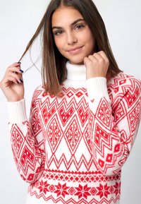 Suéter de patrón rojo y blanco con un cuello alto tipo tortuga. Presenta diseños geométricos y florales en secciones alternas. Textura suave de punto.
