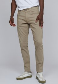 Pantalons en coton beige avec une coupe slim, dotés de poches avant et de passants de ceinture. Associés à des baskets blanches et beiges.