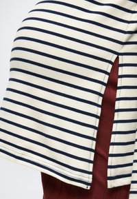 Υφασμα με λευκές και ναυτικές ρίγες και πλευρική σχισμή που αποκαλύπτει σκούρο κόκκινο υφασμα με ριμπ υφή από κάτω.