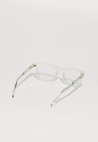 Gafas rectangulares transparentes con montura de plástico transparente y brazos elegantes. Presentan sutiles acentos metálicos en la bisagra. Las lentes son claras.