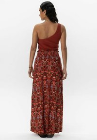 Haut côtelé rouille à une épaule associé à une longue jupe maxi à motifs avec des designs géométriques rouges, violets et verts. Taille élastique.