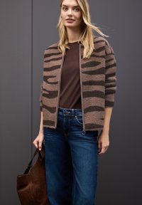 Brun och svart randig fluffig kofta över en brun topp, kombinerad med blå vida jeans och en brun mockaväska.