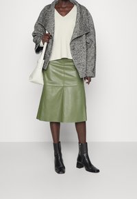 Grå tweedkappa, beige ribbad topp, grön läderkjol och svarta ankelstövlar. Kjolen är knälång med en slät yta. Vit handväska.