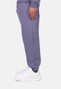 Light purple jogger pants made of soft fabric, featuring an elastic waistband and cuffed ankles, paired with white athletic shoes.