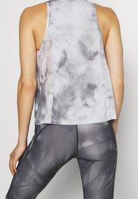 Top senza maniche grigio con un motivo che ricorda le nuvole, caratterizzato da una vestibilità ampia e una leggera lucentezza, abbinato a leggins scuri con un motivo geometrico.