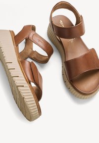 Sandalias de cuero marrón con tiras anchas ajustables y suelas gruesas beige acanaladas para mayor comodidad y soporte.