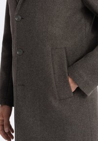 Manteau en laine gris foncé avec une finition texturée, doté d'une fermeture à deux boutons, de poches latérales et d'une coupe ajustée.