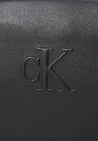 Black leather bag featuring embossed initials "cK" prominently displayed. The surface has a textured finish with a sleek design.