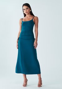 Teal värinen maksi mekko ohuilla spagettiolkaimilla, kerrostettu yksityiskohta vyötäröllä ja sivussidoksia. Sujuva, kevyt kangas ja levenevä helma.