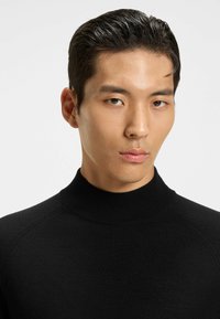 Maglione nero a collo alto, con una texture a maglia liscia e maniche raglan. Il tessuto appare morbido e aderente.