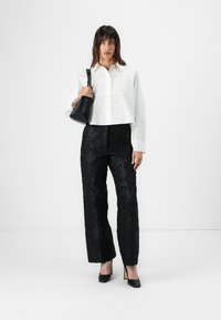 White cropped button-up shirt, black textured floral wide-leg pants, black high heels, and a small black handbag. Plain background.