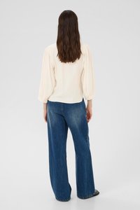 Blouse couleur crème, ample, avec des manches bouffantes, associée à un jean large bleu. Texture de tissu lisse, design décontracté avec une coupe décontractée.