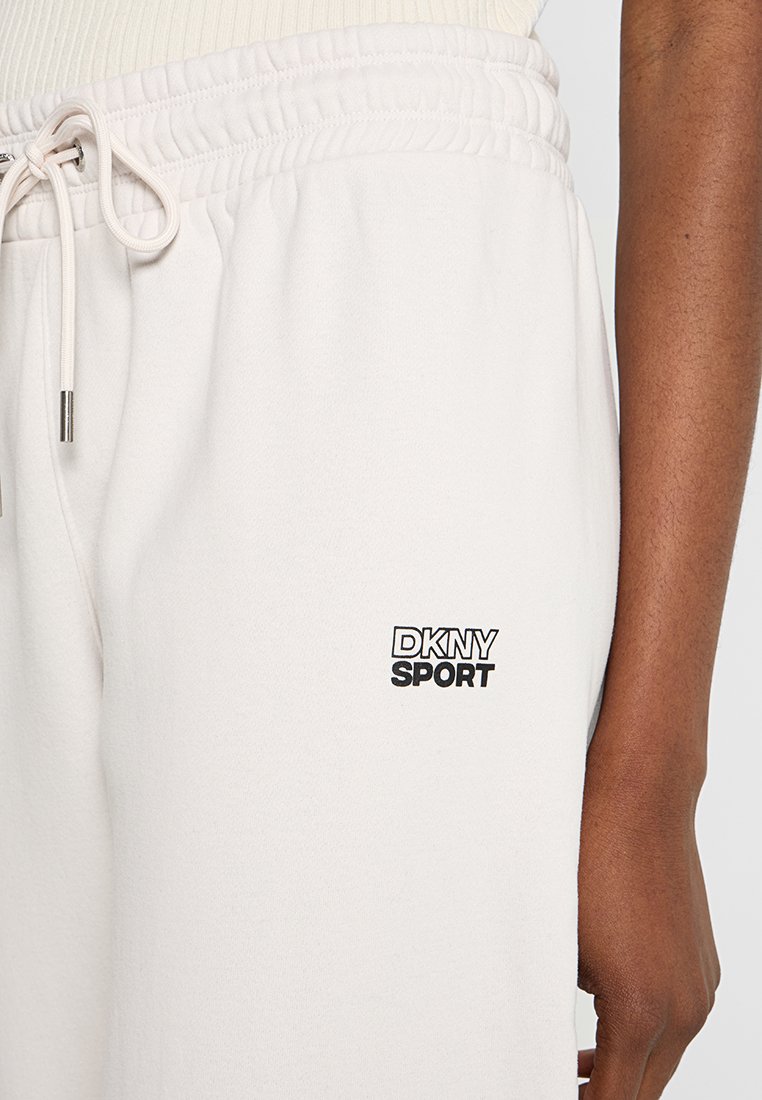 Jasnobeżowe dresy DKNY Sport mają elastyczny pas ze sznurkiem, elastyczne mankiety i małe czarne logo na lewym udzie. Gładka tekstura.