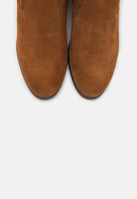 Bottines en daim marron avec une texture lisse, un bout arrondi et des détails de couture minimaux ; semelles en caoutchouc plates offrant stabilité.