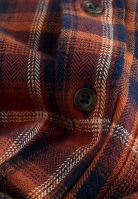 Orange og marineblåt ternet stof med en blød tekstur. Har vævede mønstre og en rund brun knap med "Superdry" indgraveret.