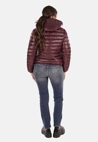 Giacca a vento bordeaux con colletto alto, design trapuntato e finitura lucida, abbinata a jeans attillati blu scuro e scarpe con plateau nere.