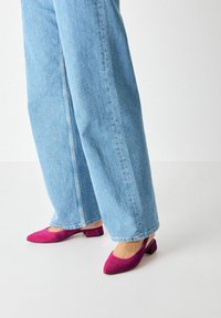 Fuchsiové lodičky s otevřenou patou a nízkým blokovým podpatkem, v kombinaci se světle modrými kalhotami s širokými nohavicemi, vytvářející ležérní vzhled.