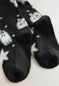Calcetines negros hasta el tobillo con patrones de fantasmas y estrellas en plata; textura acanalada; punta redondeada; el tejido parece suave y elástico.