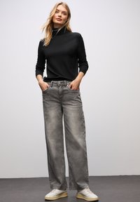 Maglione nero a collo alto con maniche lunghe abbinato a jeans larghi grigi chiari. Sneakers bianche completano l'outfit, caratterizzate da una texture liscia.