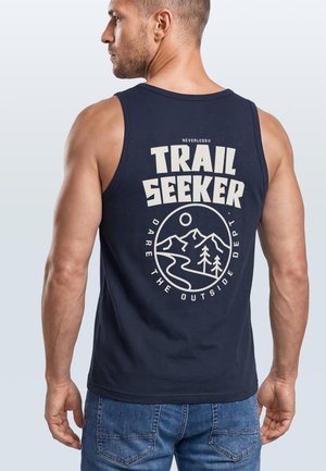 Mann trägt ein dunkelblaues ärmelloses Shirt mit dem Schriftzug „Trail Seeker“ und einer Grafik von Berg, Bäumen und einem Weg auf dem Rücken.