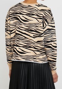 Beige sweatshirt med svart och vit zebra rand. Har en rundad hals och ribbade muddar. Matcher med en veckad svart kjol.