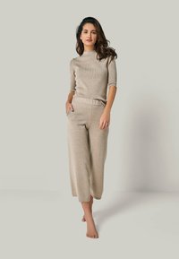 Beiger, gerippter Strickpullover mit kurzen Ärmeln und hohem Ausschnitt, kombiniert mit passenden beige-weiten Hosen mit elastischem Bund und Taschen.