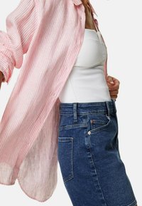 Lichtroze en witte gestreepte button-up blouse, gelaagd over een fitted witte tanktop, gecombineerd met een donkere blauwe denim rok.
