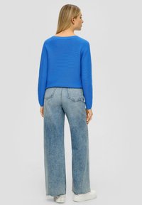 Blauer Strickpullover mit Rundhalsausschnitt, kombiniert mit hellblauen, hochtailliertenweiten Jeans und weißen Plateausneakern.