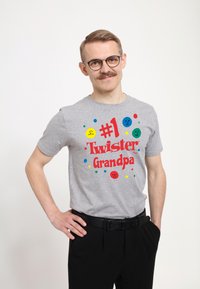 Šedé bavlněné tričko s červeným nápisem "#1 Twister Dědeček" a barevnými úsměvnými obličeji. Nosené s černými kalhotami, jednoduchý kulatý výstřih.
