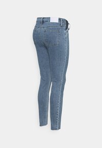 Jeans skinny de denim azul com uma cintura de altura média, cinco bolsos e uma textura suave. Apresenta um cós em contraste e detalhes de costura discretos.