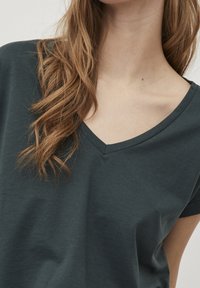 Tmavě zelené bavln�ěné tričko s výstřihem do V, krátkými rukávy, hladkou texturou a minimálními detaily šití.