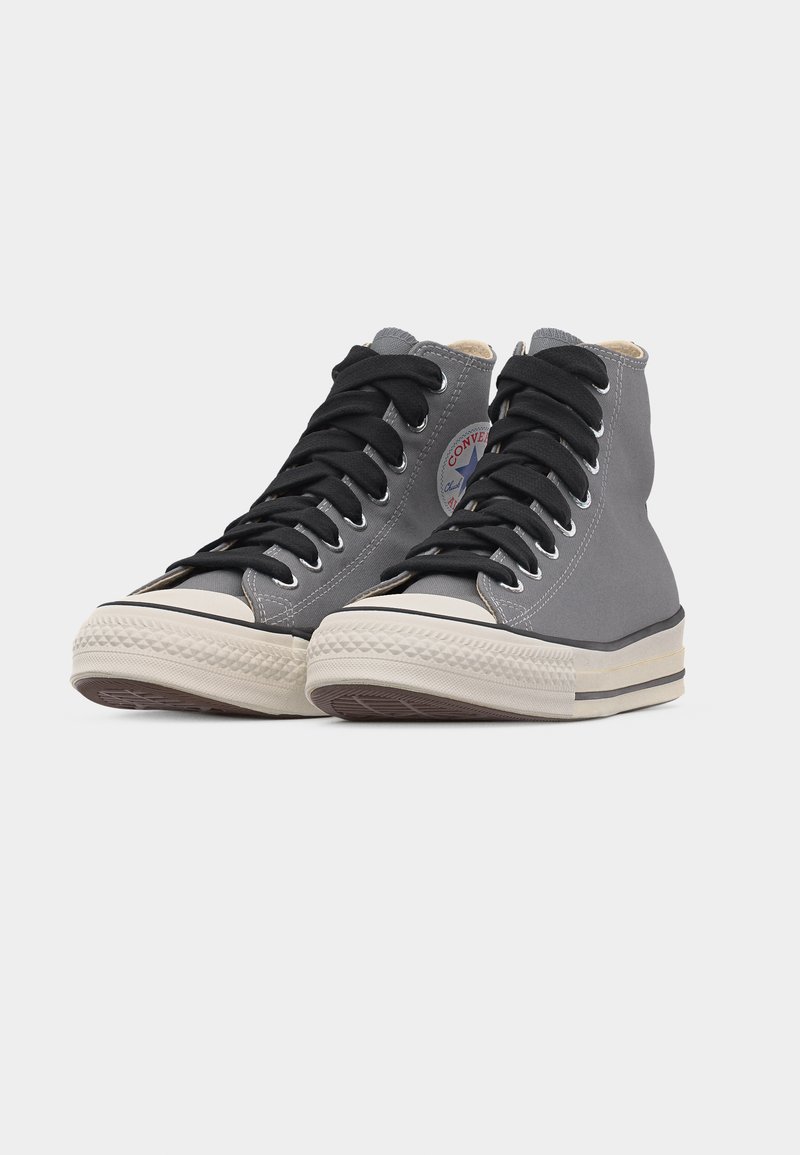 Coppia di sneaker alte in tela grigia con lacci neri e suole in gomma bianche su sfondo chiaro uniforme.