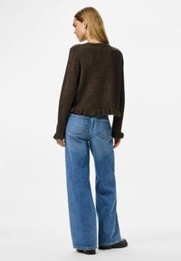 Brun kortärmad tröja med volang nertill, tillsammans med blå vida jeans. Jeansarna har bakfickor och rak skärning.