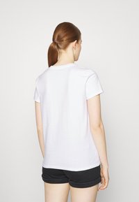 White, short-sleeve t-shirt with a rounded neckline. Soft cotton material, straight hem, and a relaxed fit. Worn with black shorts.