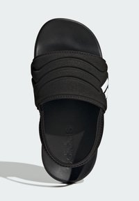 Černá pantofle na klínu s texturovanou stélkou, širokým polstrovaným páskem s vroubkováním a bílým logem. Materiál působí synteticky a pružně.