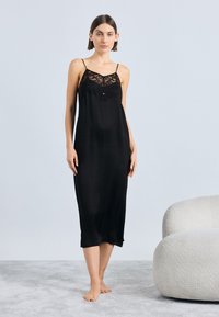 Rochie neagră slip din material mătăsos, cu detalii din dantelă la decolteu și bretele subțiri reglabile. Textură netedă, lungime până la jumătatea gambei.