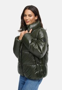 Puffjacka i mörkgrön, glänsande material med hög krage, blixtlås och sidoknappar. Visad i en avslappnad passform med quiltade detaljer.
