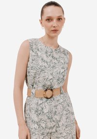 Blommönstrad ärmlös klänning i grönt och vitt, med ett brunt vävt bälte och rund spänne. Slät tyg, avslappnad passform.