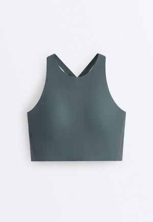 Ærmeløs, mørkegrøn sports-bh med høj halsudskæring og krydsede stropper bagpå på en hvid baggrund.