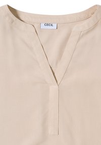 Beige bluse med V-udskæring og kort slids. Har glat stof med minimale syninger. Mærket viser "CECIL."