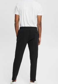 Czarne elastyczne spodnie o dopasowanym kroju, z elastycznym paskiem w talii i tylnymi kieszeniami, zestawione z prostą białą koszulką i białymi trampkami.