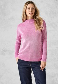 Rosa ribbad långärmad tröja med hög hals och Texturvariationer. Tillsammans med mörkblå jeans. Inga synliga logotyper eller mönster.