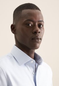 Camicia azzurra chiara con sottili righe bianche, colletto a bottoni, tessuto strutturato e vestibilità sagomata. Nessun logo o motivo visibile.