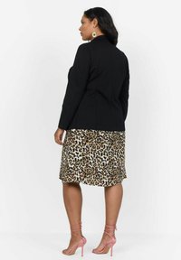 Černý přizpůsobený blazer přes šaty s leopardím potiskem, se splývavým spodním lemem. Růžové sandály na tenkých podpatcích dokreslují outfit. Hladké materiály a kontrastní vzory.