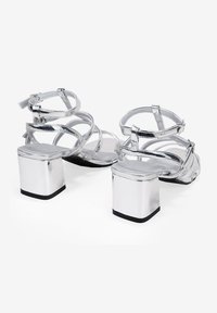 Sandalias plateadas con tacón cuadrado y múltiples correas. Acabado metálico liso, talón cerrado y plantilla plana.