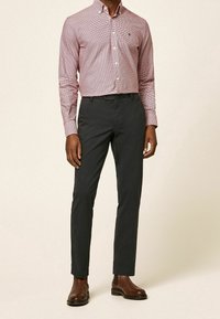 Czerwona i biała koszula w kratę z długim rękawem i kołnierzykiem na guziki, zestawiona z ciemnoszarymi, dopasowanymi spodniami i brązowymi botkami za kostkę.